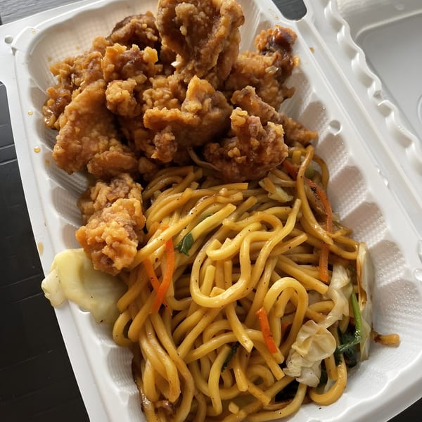 Crispy fried chicken and stir-fried noodles with vegetables in a white takeout container.