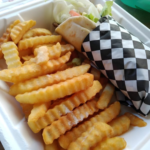 A Mgwalexs Hawaiian Grill gyro wrapped in checkered paper, alongside crinkle-cut fries in a white container.