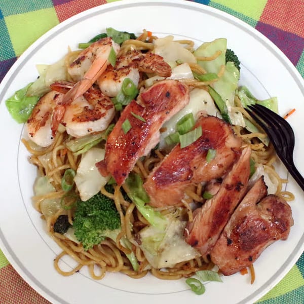Hawaiian plate lunch with grilled chicken, shrimp, noodles, and vegetables on a white plate.