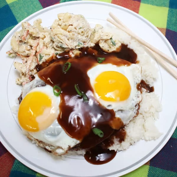 Hawaiian Loco Moco with two fried eggs, gravy, rice, and macaroni salad on a white plate.