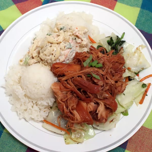 Hawaiian plate lunch with kalua pig, rice, macaroni salad, and cabbage on a white plate.